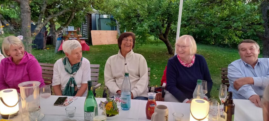 Fünf Chormitglieder sitzen abends lachend an der langen Gartentafel