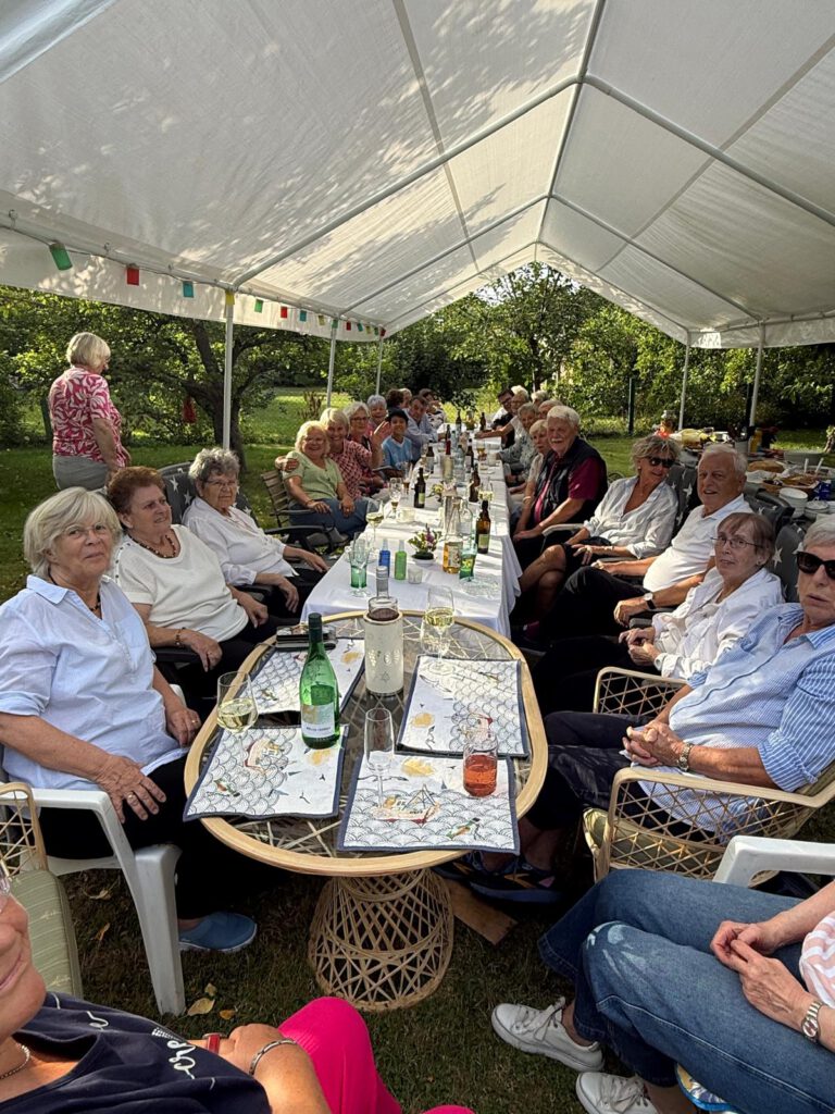 Die Chorgemeinschaft sitzt an der langen Tafel unter dem Zeltdach