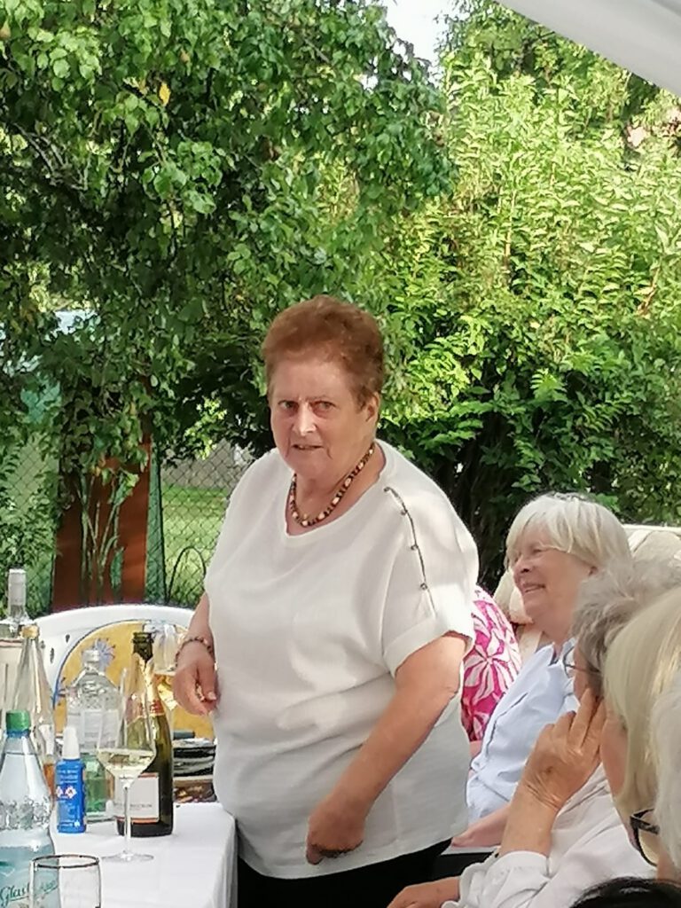 Rosi steht bei ihrer Darbietung im Garten, umgeben von lachenden Gästen