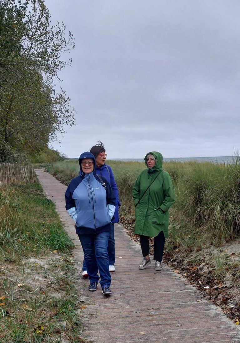 Drei Sängerinnen in Regenjacken auf dem Bohlenweg durch die Dünen